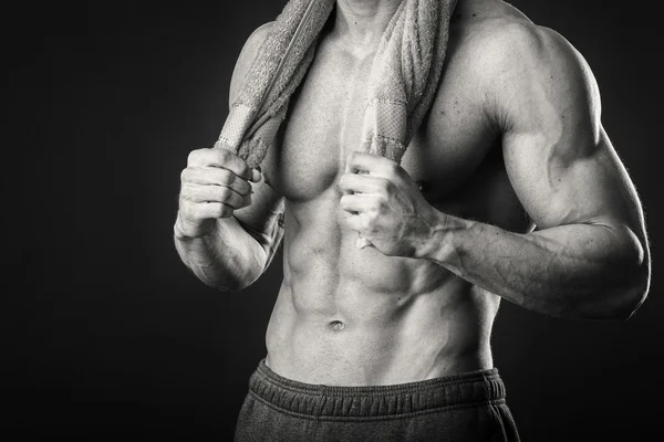 Muskulös man med en handduk i händerna på en mörk bakgrund — Stockfoto