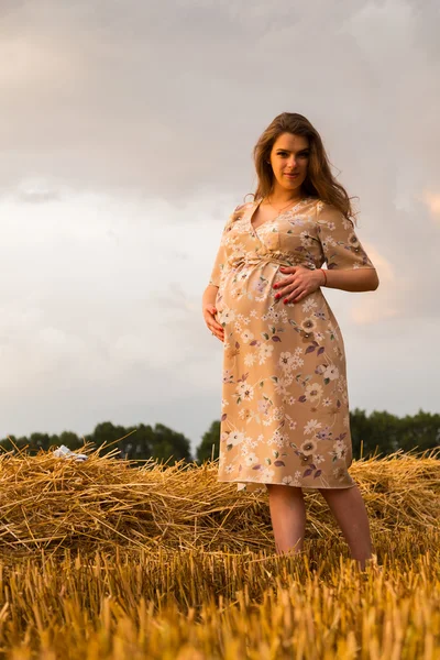 Een jonge man en een zwangere vrouw zitten in een tarweveld van vers gesneden tarwe — Stockfoto