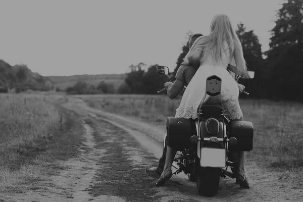 Homem musculoso com uma mulher bonita em uma motocicleta no meio de uma estrada de campo — Fotografia de Stock