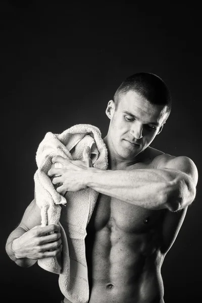 Homem musculoso com uma toalha nas mãos sobre um fundo escuro — Fotografia de Stock