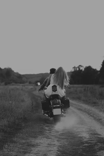 Hombre musculoso con una mujer hermosa en una motocicleta en medio de un camino de campo — Foto de Stock