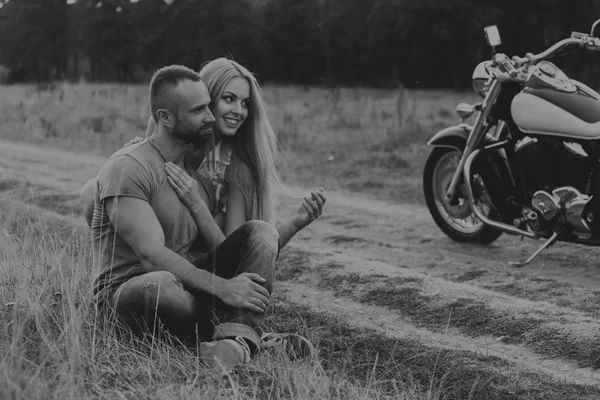 Muscular man with a beautiful woman on a motorcycle middle of a field road