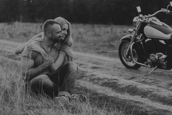 Hombre musculoso con una mujer hermosa en una motocicleta en medio de un camino de campo — Foto de Stock