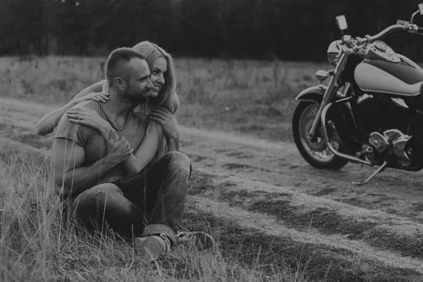 Homem musculoso com uma mulher bonita em uma motocicleta no meio de uma estrada de campo — Fotografia de Stock