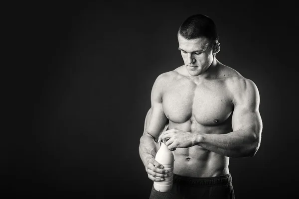 Bodybuilder mit einer Flasche Milch auf dunklem Hintergrund — Stockfoto