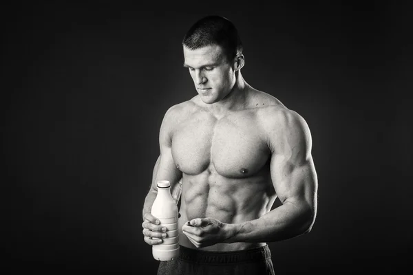 Bodybuilder mit einer Flasche Milch auf dunklem Hintergrund — Stockfoto