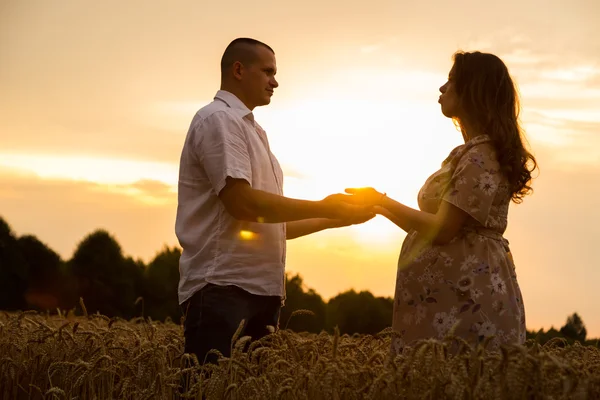 Un jeune homme et une femme enceinte assis dans un champ de blé de blé fraîchement coupé — Photo