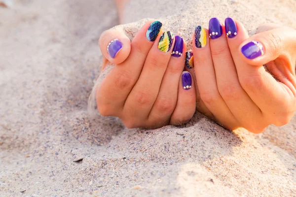 Beautiful women's hands with bright manicure on a sea of sand — Stock Photo, Image