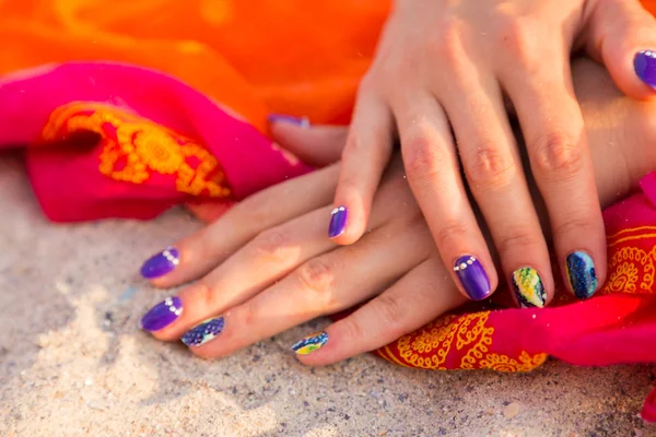 Mãos de mulher bonitas com manicura brilhante em um mar de areia — Fotografia de Stock