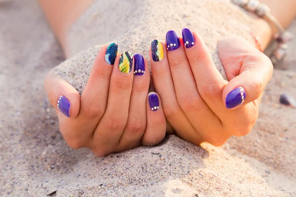 Belles mains de femmes avec manucure lumineuse sur une mer de sable — Photo