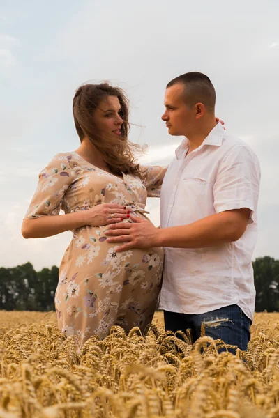 Un jeune homme et une femme enceinte assis dans un champ de blé de blé fraîchement coupé — Photo