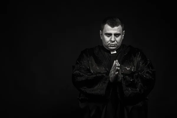 A professional stage actor in the guise of a priest against a dark background