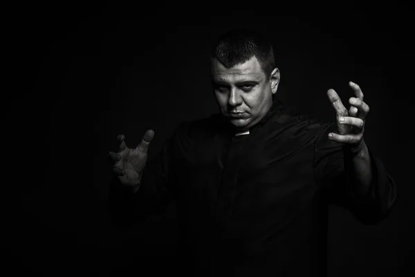 A professional stage actor in the guise of a priest against a dark background