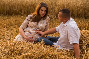 Genç bir adam ve taze kesilmiş buğday buğday tarlasında oturan bir hamile kadın