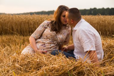 Genç bir adam ve taze kesilmiş buğday buğday tarlasında oturan bir hamile kadın