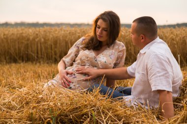 Genç bir adam ve taze kesilmiş buğday buğday tarlasında oturan bir hamile kadın