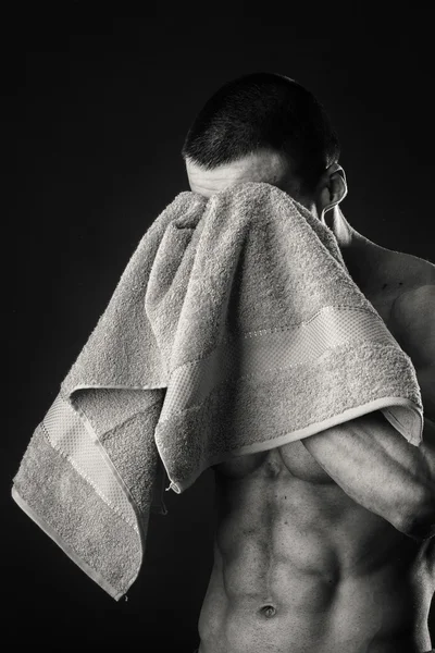 Muskulös man med en handduk i händerna på en mörk bakgrund — Stockfoto