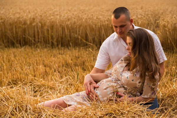 Egy fiatal férfi és egy terhes nő ül egy Búzamező, frissen vágott búza — Stock Fotó