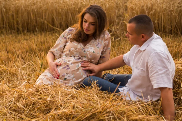 Een jonge man en een zwangere vrouw zitten in een tarweveld van vers gesneden tarwe — Stockfoto