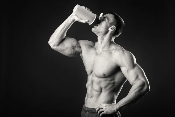 Muskulöser Mann mit einem Shaker in der Hand vor dunklem Hintergrund — Stockfoto