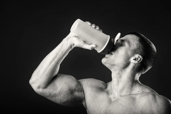Uomo muscolare con uno shaker in mano su uno sfondo scuro — Foto Stock