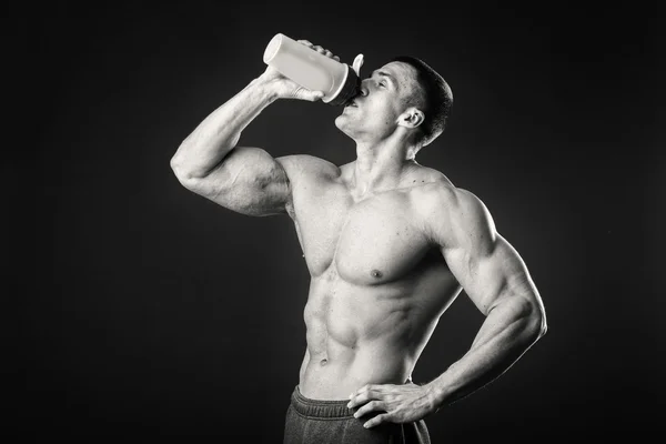 Muskulöser Mann mit einem Shaker in der Hand vor dunklem Hintergrund — Stockfoto