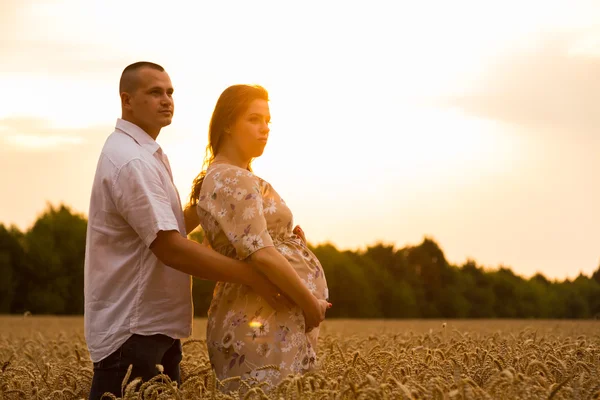 Um jovem e uma mulher grávida sentados em um campo de trigo de trigo recém-cortado — Fotografia de Stock