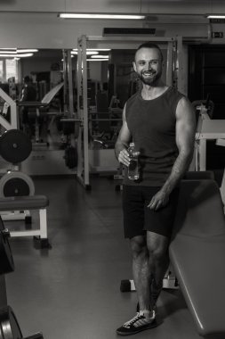 Spor salonunda güçlü bir adam. Egzersizler arasında bekletin. Yakışıklı adam su içer.
