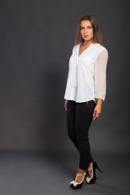 Şık giyimli genç iş kadını. Güzel genç iş kadını görüntüsü. Kız siyah pantolon ve karanlık bir arka plan üzerinde beyaz bir gömlek. Moda ve sosyal dergiler, Web siteleri için fotoğraf.