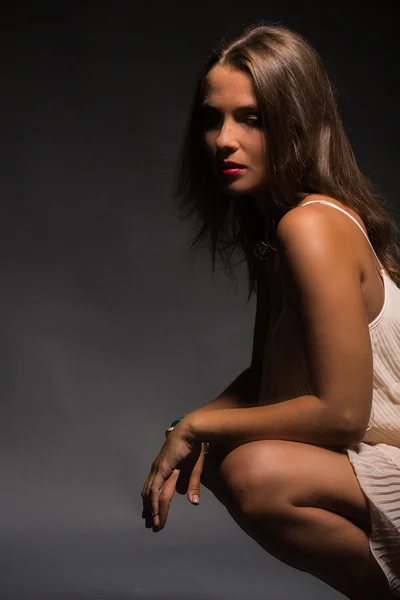 The romantic image of the beautiful brunette in a delicate white dress against a dark background. — Stock Photo, Image