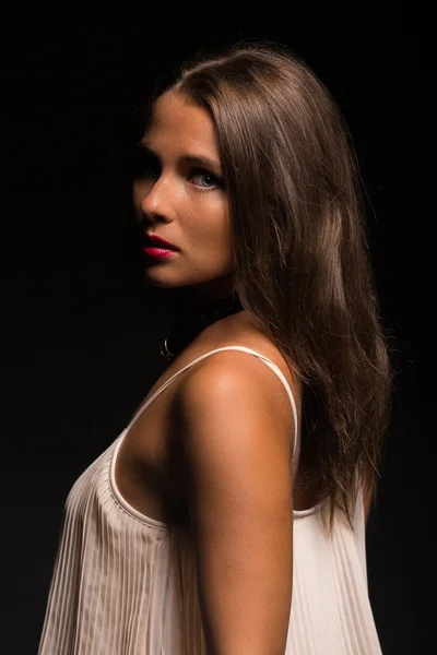 The romantic image of the beautiful brunette in a delicate white dress against a dark background. — Stock Photo, Image