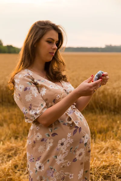 Uma mulher grávida num campo de trigo. Uma mulher feliz no terreno. A mulher alegra o feto. Emoções sinceras e sentimento de alegria. Bela paisagem rural. Campo de trigo aguardando colheita . — Fotografia de Stock