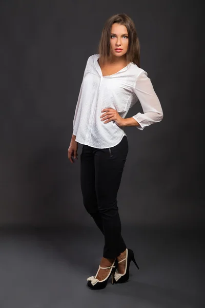 Stylishly dressed young business lady. The image of a beautiful young business lady. Girl in black pants and a white shirt on a dark background. Photo for fashion and social magazines, websites. — Stock Photo, Image