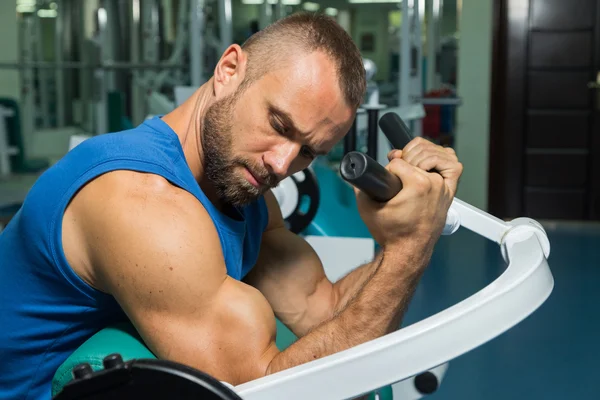 The athlete does bench biceps on the simulator in the gym. Hand muscle training on the simulator. Tense muscles of hands under load. Photos for sporting magazines, posters and websites. — Stock Photo, Image