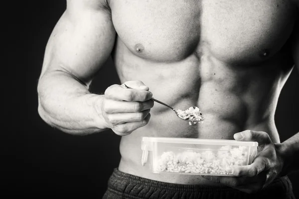 Muskulöser Mann isst Quark auf dunklem Hintergrund. — Stockfoto