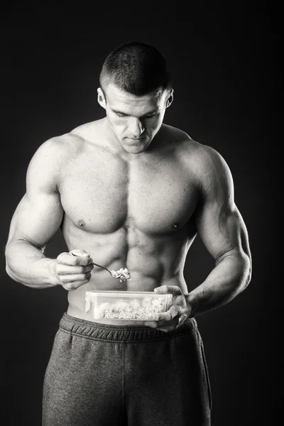 Musclé homme mange fromage cottage sur un fond sombre . — Photo