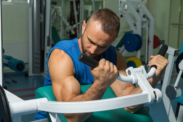 El atleta hace bíceps de banco en el simulador en el gimnasio. Entrenamiento muscular de mano en el simulador. Los músculos tensos de las manos bajo carga. Fotos para revistas deportivas, carteles y sitios web . —  Fotos de Stock