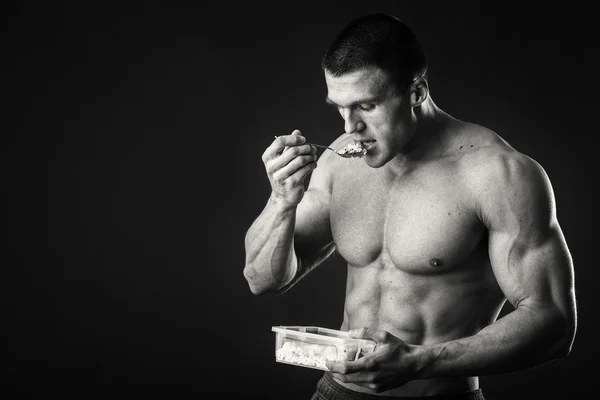 Hombre musculoso come queso cottage sobre un fondo oscuro . —  Fotos de Stock