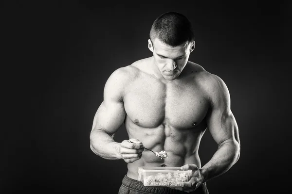 Homem muscular come queijo cottage em um fundo escuro . — Fotografia de Stock