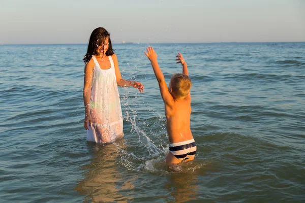 Young mother with son playing in the sea. A beautiful young mother and little boy happy gaming in water. Family holidays at sea. Photo for family and social magazines, posters and websites. — Stock Photo, Image