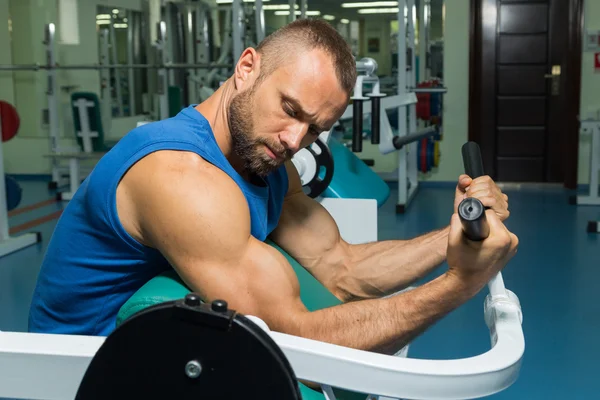 Sportowiec ława biceps w symulatorze siłowni. Trening mięśni ręki na symulatorze. Napięte mięśnie rąk pod obciążeniem. Zdjęcia sportowe czasopisma, plakaty i stron internetowych. — Zdjęcie stockowe