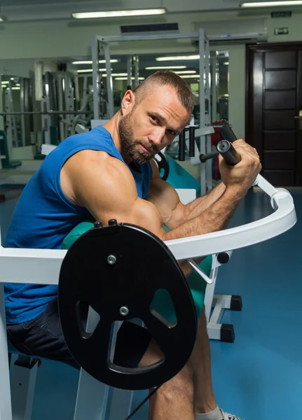 L'athlète fait des biceps de banc sur le simulateur dans la salle de gym. Entraînement musculaire des mains sur le simulateur. Muscles tendus des mains sous charge. Photos pour magazines sportifs, affiches et sites web . — Photo