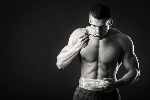 Muskulöser Mann isst Quark auf dunklem Hintergrund. — Stockfoto