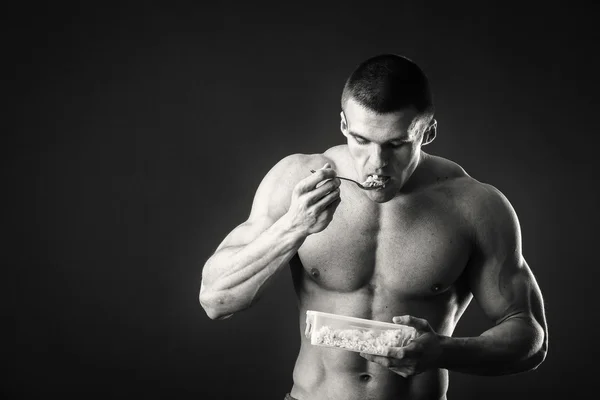 Muskulöser Mann isst Quark auf dunklem Hintergrund. — Stockfoto