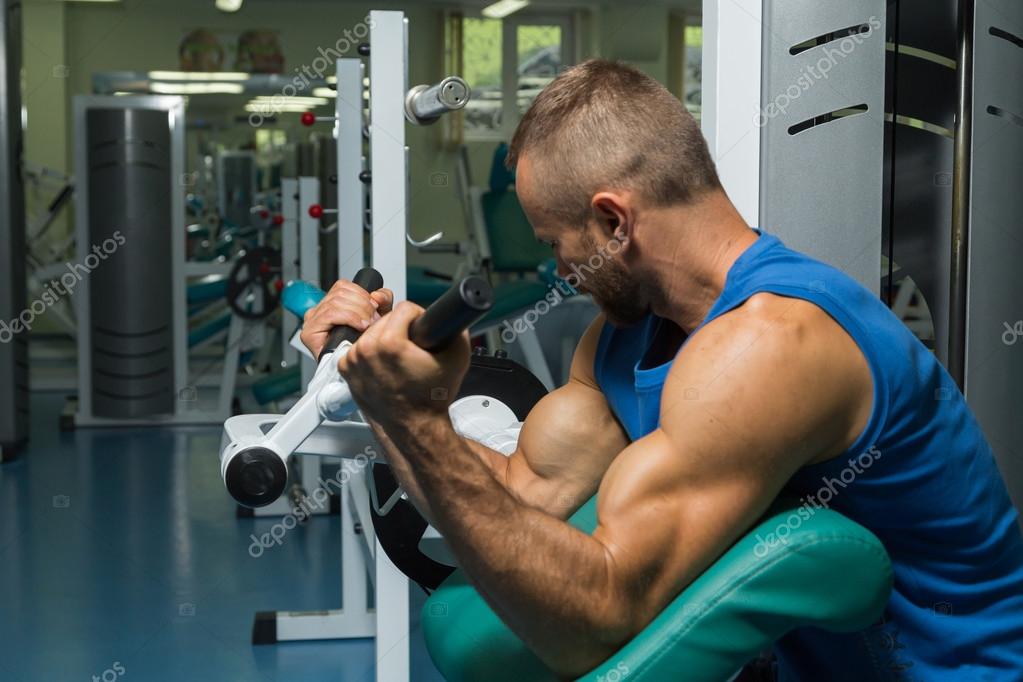 The athlete does bench biceps on the simulator in the gym. Hand muscle training on the