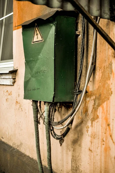 green electrical distribution box hanging on a ragged wall