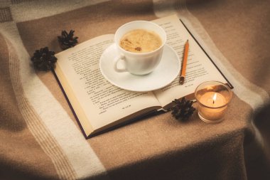 Bir kitap ve bir fincan kahveyle kış sıcacık kompozisyonu, krema renginde hayat, tarz ve sakin ruh hali fotoğrafı.