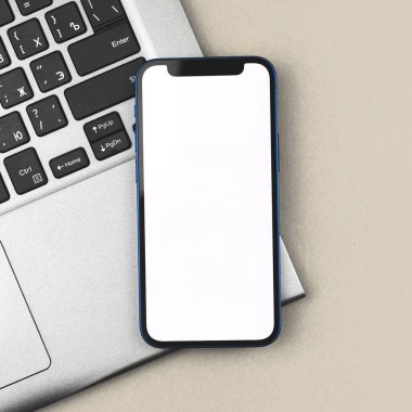 Boş beyaz ekranlı cep telefonlu iş modeli, arka planda dizüstü bilgisayar