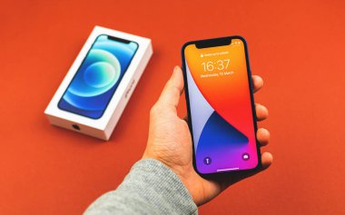 Kharkov, Ukrayna - 12 Mart 2021: Yepyeni bir iPhone 12 taşıyan ve perakende satış kutusunun arka planında kilitli ekranı olan adam, satın alma kavramı
