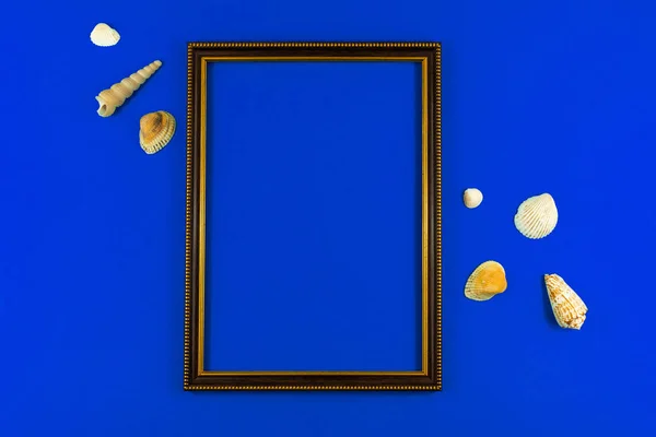 Summer flat lay composition with wooden frame and seashell on a blue background, copy space and top view